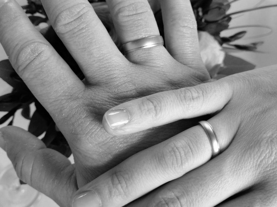 Zwei übereinander liegende rechte Hände, die jeweils am Ringfinger einen schlichten Ring tragen